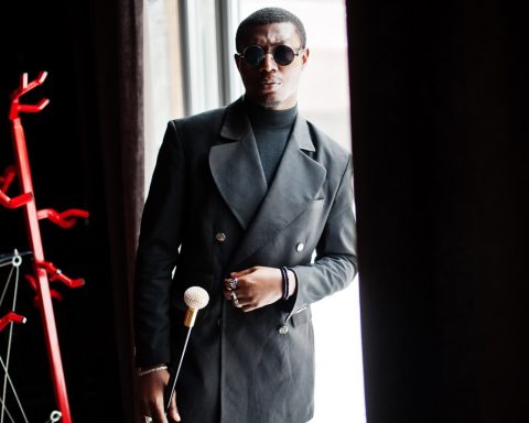 Stylish african american gentleman in elegant black jacket and sunglasses, holding retro walking stick as cane flask or tippling cane with golden diamond ball handle. Rich fashionable afro man.